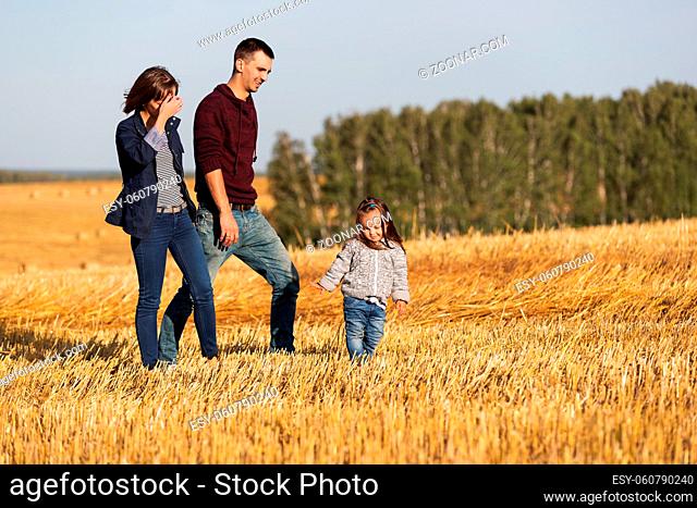 Happy young family with two year old girl walking in a harvested field