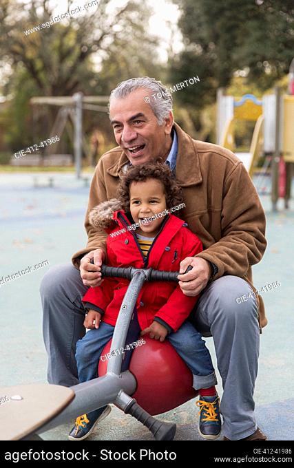 Grandfather playing with grandson on playground seesaw