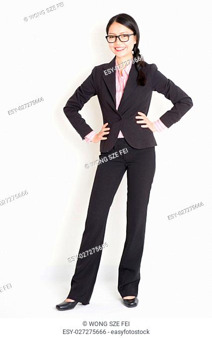 Full body portrait of young Asian businesswoman in formalwear hands on waist and smiling, standing on plain background