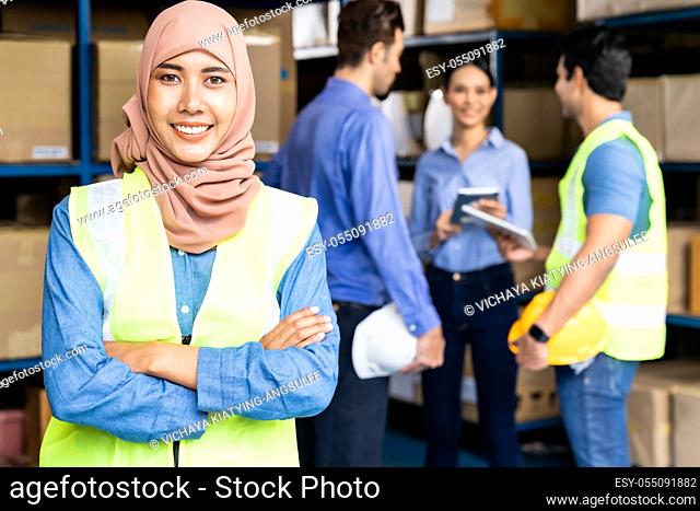 Portrait of Islam Muslim female warehouse worker crossed arm with her colleagues meeting in warehouse distribution center environment