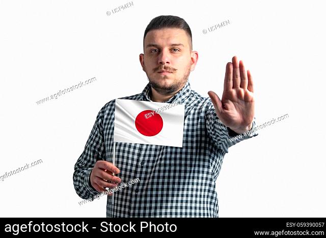 White guy holding a flag of Japan and with a serious face shows a hand stop sign isolated on a white background