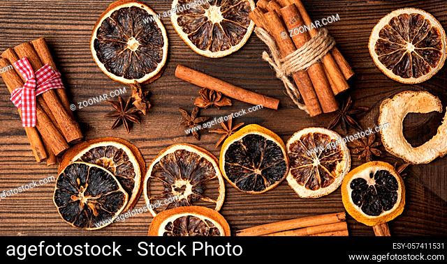 cinnamon sticks and dry orange slices on brown wooden board, top view