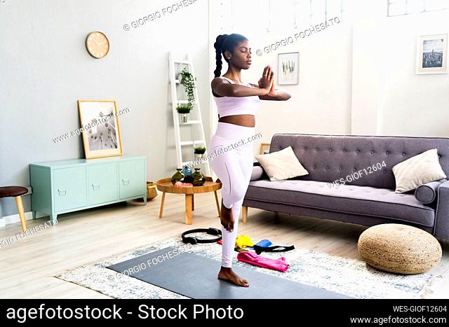 Young woman standing on one leg while doing yoga at home