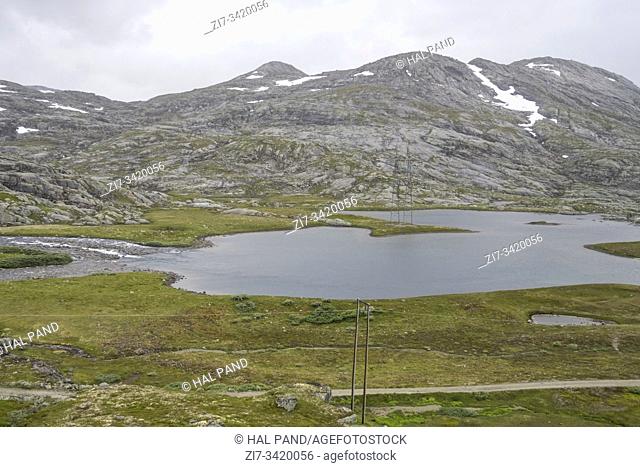 landscape with dirt road near lake in high valley on barren mountains with some summer snow, shot under bright cloudy summer light near Finse, Norway