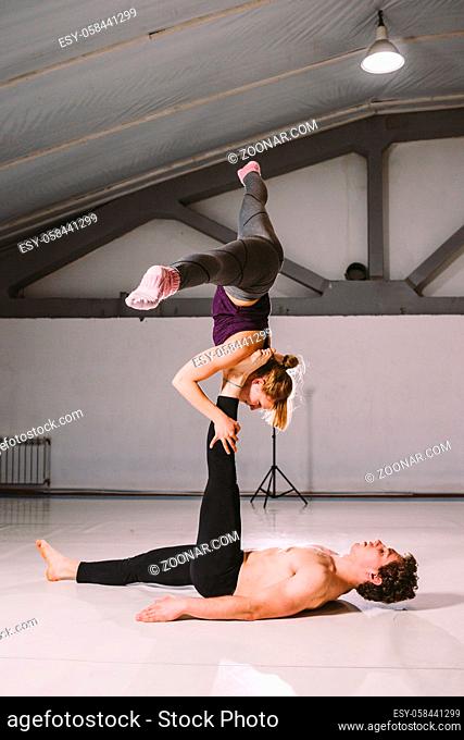 Theme sport and a healthy lifestyle. Acrobatics and acroyoga. Young sporty couple practicing acroyoga handstand. Male and female acrobats doing together Acro...