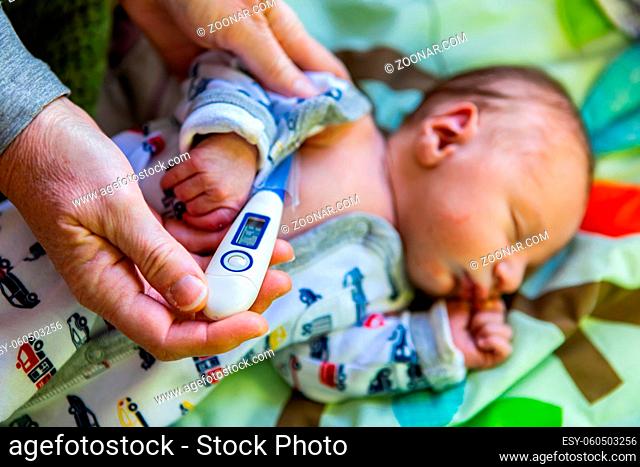 A close up selective focus view on the hands of a family doctor using a medical thermometer under the arm of a newborn baby boy, with copy space