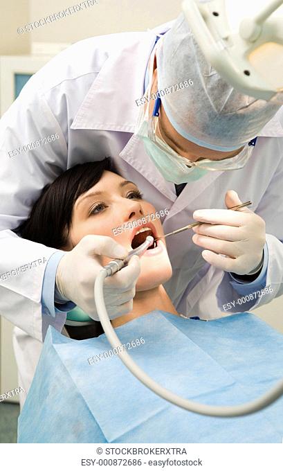 Vertical image of female patient with dentist over her checking up teeth and drilling them
