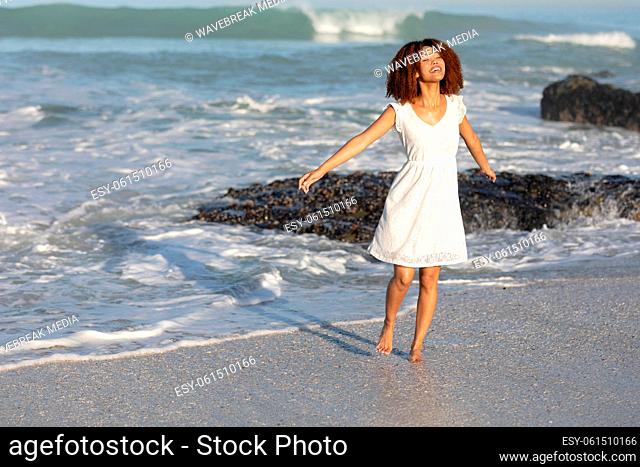A mixed race woman with her arms outstretched on beach on a sunny day