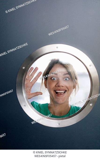 Portrait of woman pulling funny faces behind porthole