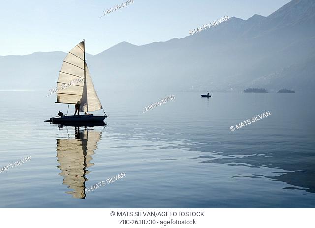 Sailing boat reflected on alpine lake Maggiore with Brissago islands and mountain in Ascona, Switzerland