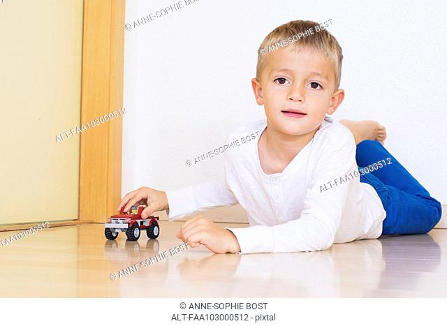 Boy lying on floor playing with toy truck
