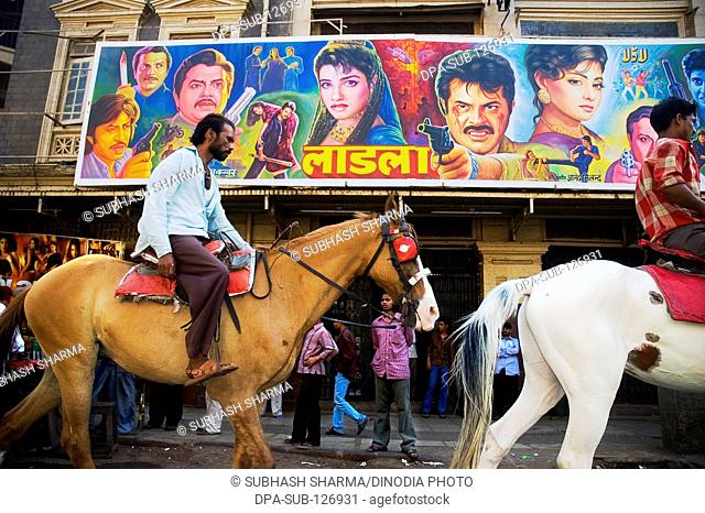 Bollywood horse supplier riding horse in front of Bollywood poster at Alfred Cinema; Grant Road; Bombay Mumbai ; Maharashtra ; India