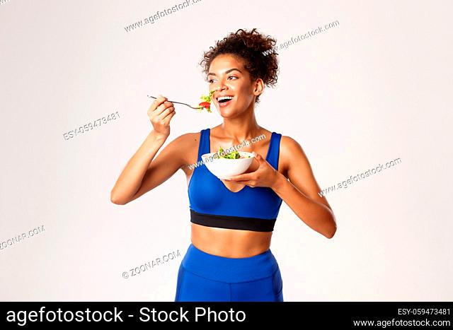 Healthy lifestyle and sport concept. Fit attractive african-american sportswoman in blue sport outfit, eating salad and smiling