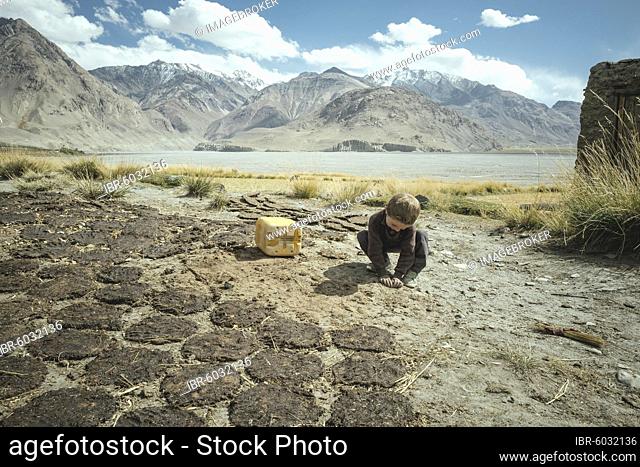 Boy plays next to cow dung flat cakes, sedentary Wakhi, behind it the mountains of the Hindu Kush, Wakhan Corridor, Saradh-e-Broghil, Afghanistan, Asia