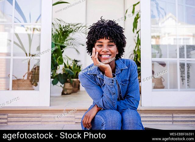 Happy woman with hand on chin sitting in front of door