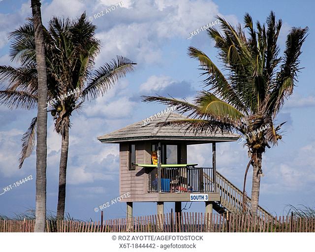 Lifeguard tower at the beach flanked by two palm trees on a sunny day with a few clouds in the sky