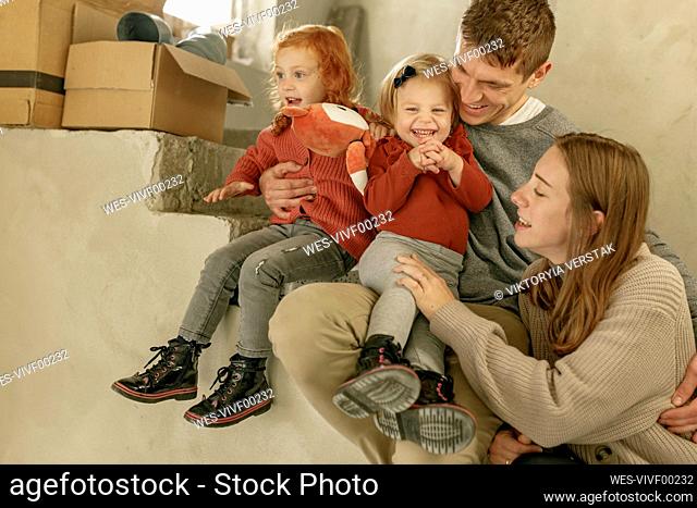 Cute happy girls sitting with parents on staircase at home