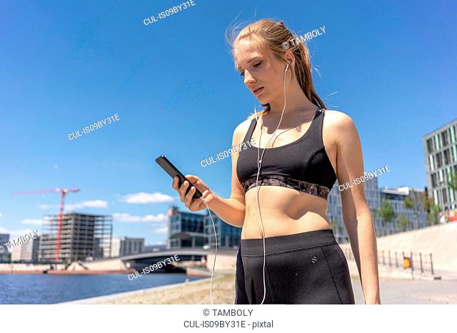 Young woman taking break from exercise and using smartphone in city, Berlin, Germany