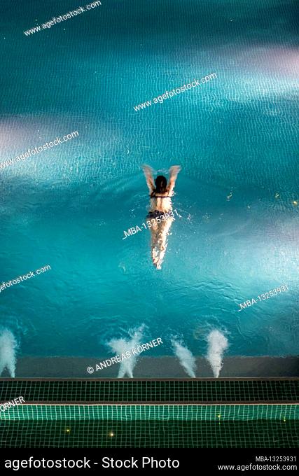 Young woman swims in a large pool at night