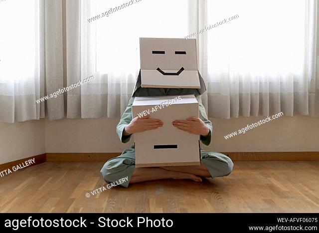Woman wearing a cardbox on head with smiley face, and closing eyes of bored smiley cardbox
