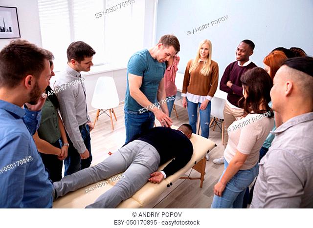 Male Instructor Teaching Massage Technique To Group Of Multi-ethnic People