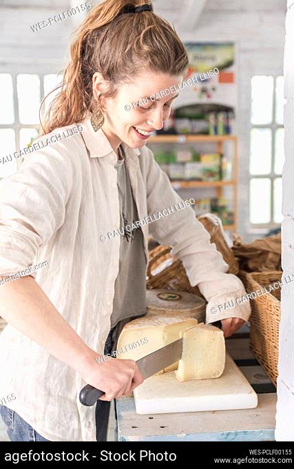 Smiling grocer cutting cheese in greengrocer shop