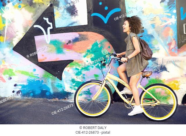 Woman riding bicycle along urban multicolor graffiti wall