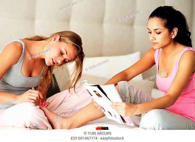 Portrait of a young girl applying nailpaint on friend nails while her friend reading magazine