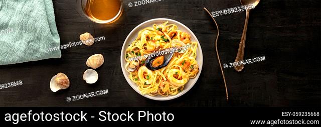 Seafood pasta panorama. Tagliolini with mussels, shrimps, clams and squids, with a glass of white wine, shot from the top on a black background with a place for...