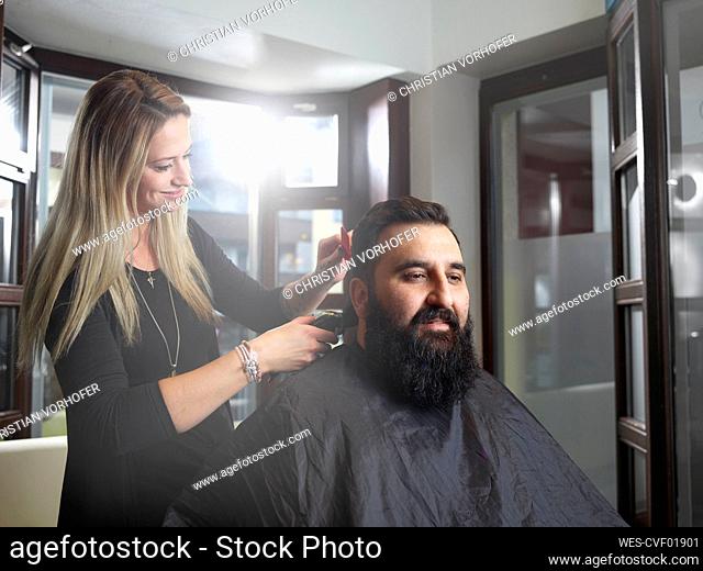 Hairstylist cutting man's hair using electric razor at salon
