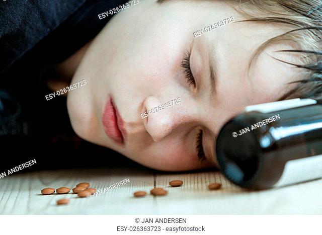 Young boy passed out on drugs and alcohol or dead after committing suicide lying on the floor with an empty medication bottle at his head and capsules around...