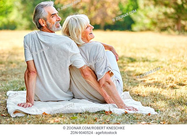 Glückliches Senioren Paar sitzt lachend auf einer Decke im Garten im Sommer