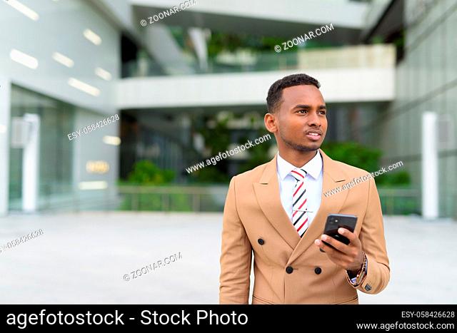 Portrait of young handsome African businessman wearing suit in the city streets outdoors