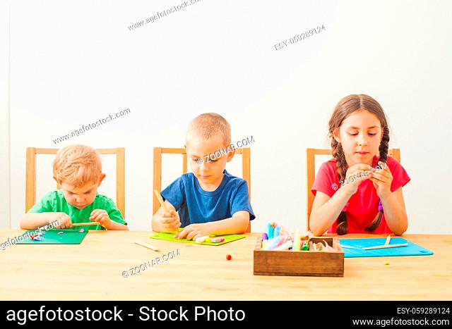 Home shcooling. Brothers and sister together play and learn molding with colorful modeling clay at the table. Children play with plasticine or dough