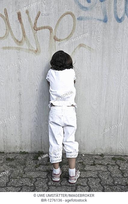 Young girl leaning against a wall, crying