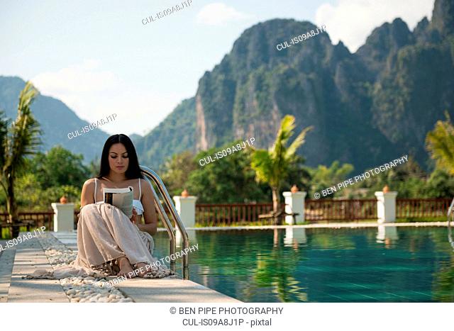 Woman sitting reading by swimming pool, Vang Vieng, Laos