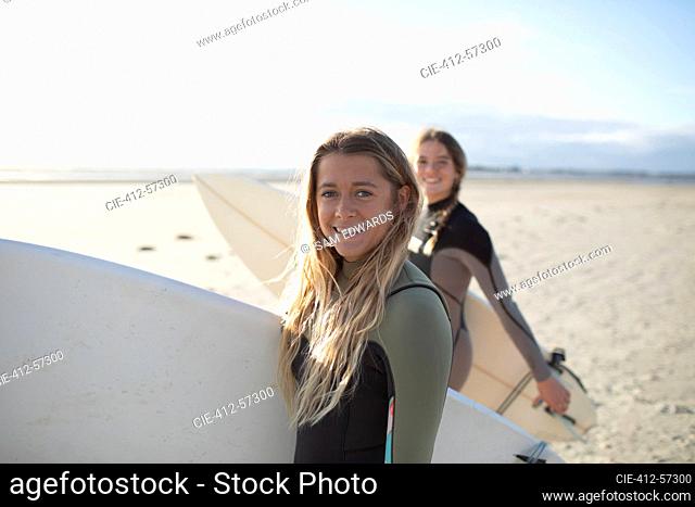 Portrait happy young female surfer with surfboard on sunny beach