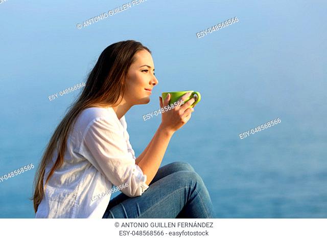 Side view portrait od a woman with a mug relaxing at sunset on the beach with a warm light