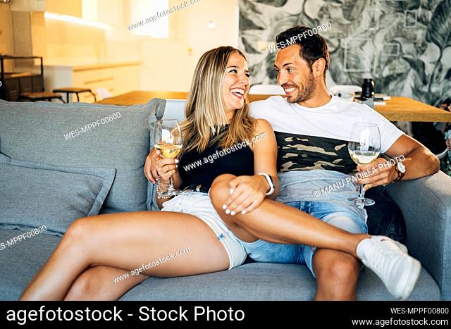 Happy couple sitting on the couch with glasses of white wine having fun