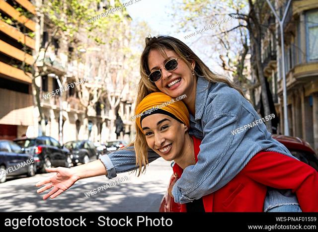 Smiling woman giving piggyback ride to female friend on sunny day