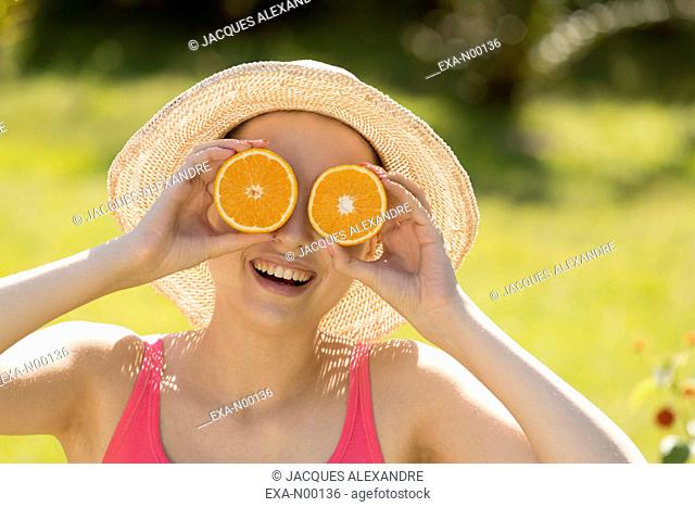 Young woman holding oranges in front of eyes