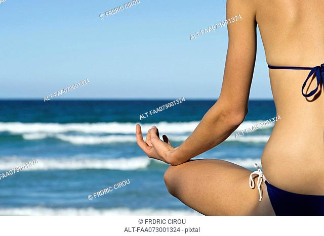 Woman in bikini sitting in lotus position by sea, rear view