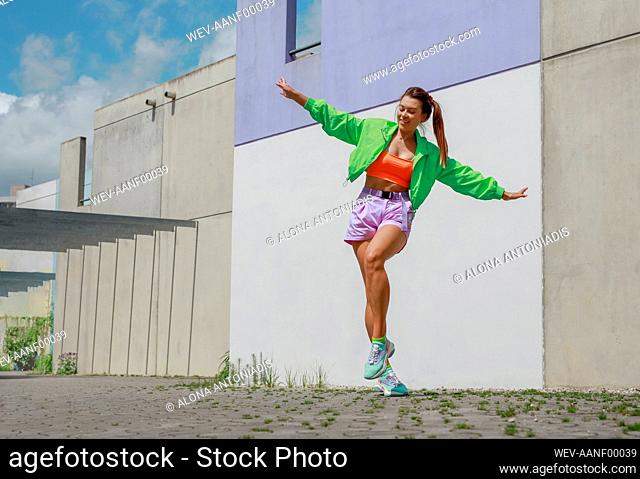 Young happy woman with arms outstretched dancing on footpath