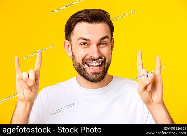 Young caucasian man wearing casual white t-shirt over yellow isolated background shouting with crazy expression doing rock symbol with hands up