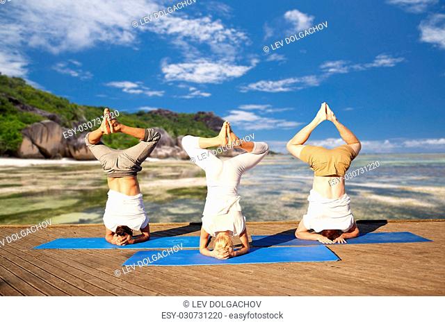 fitness, yoga and sport concept - people making headstand pose over exotic tropical beach background