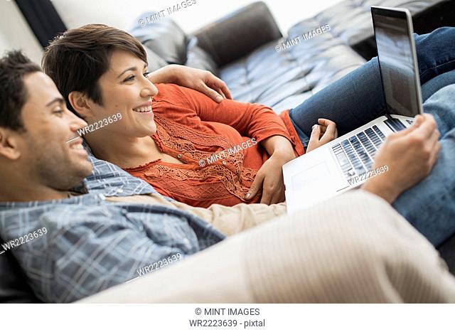 A man and woman sitting on a sofa, looking at the screen of a laptop