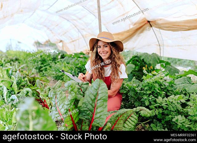 Smiling farm worker with clipboard at greenhouse