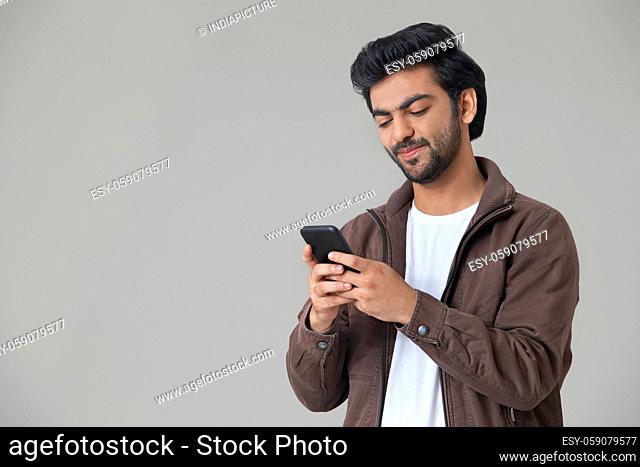 A YOUNG MAN SMILING WHILE USING MOBILE PHONE