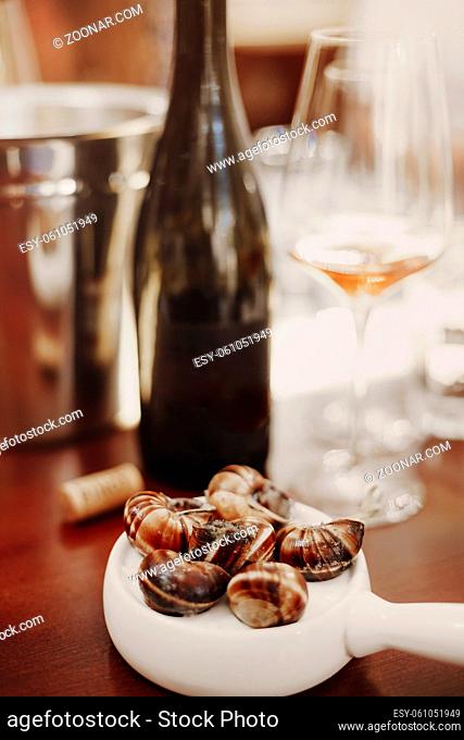 Vertical shot of escargots served on white ceramic pan alongside white wine, delicious cooked snails, enjoying traditional french cuisine in restaurant