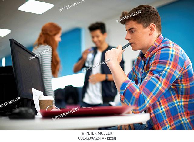 Young male college student at computer desk looking at computer